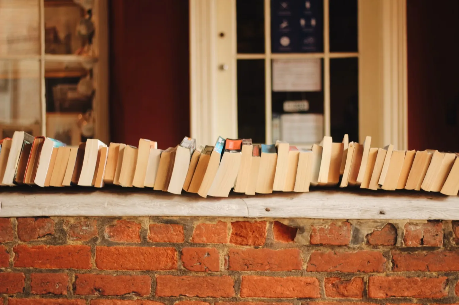 A long row of well-worn paperback books balanced along a brick window ledge.